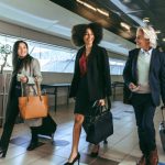 Group of multi-ethnic business people going on business trip carrying suitcases while walking through airport passageway.